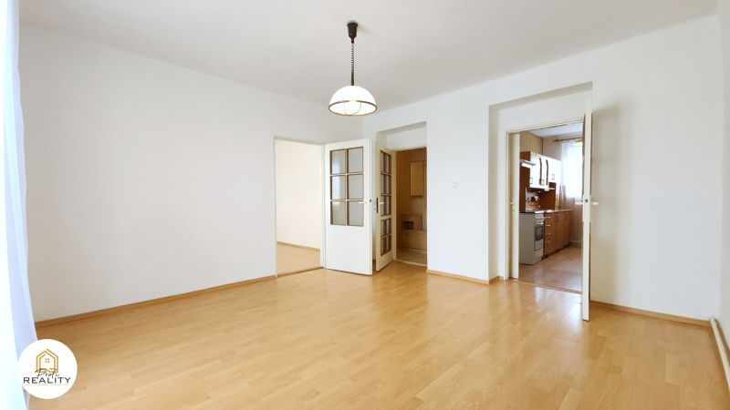 A room with a wooden floor design and entrances to the kitchen and another room.