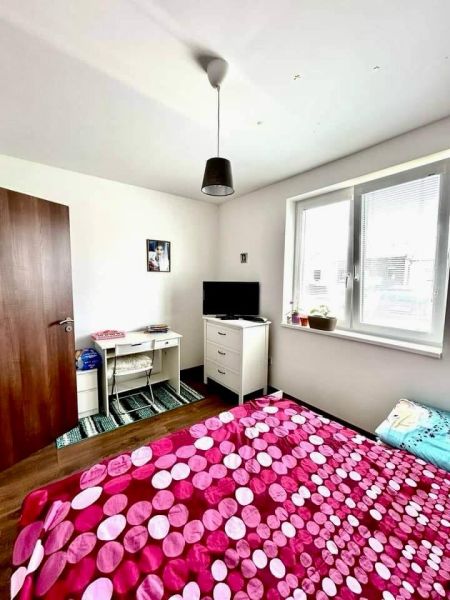 Bedroom with white furniture, colorful bed, and wooden decor flooring in a family house.