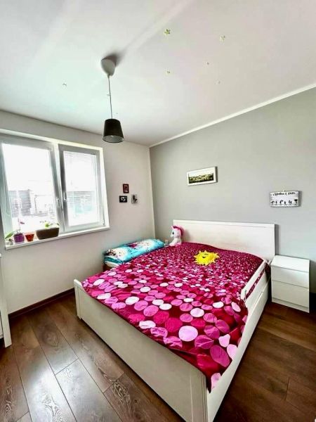 A bedroom in a family house with a wood-patterned floor, a white bed, and a pink blanket.