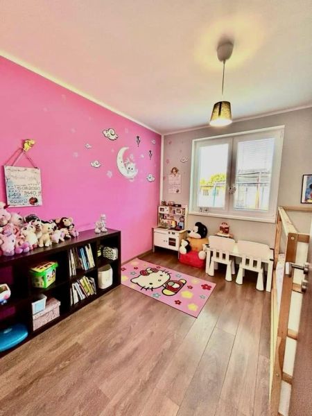 Children's room with a pink wall, toys, and a wooden decor floor in a family house.