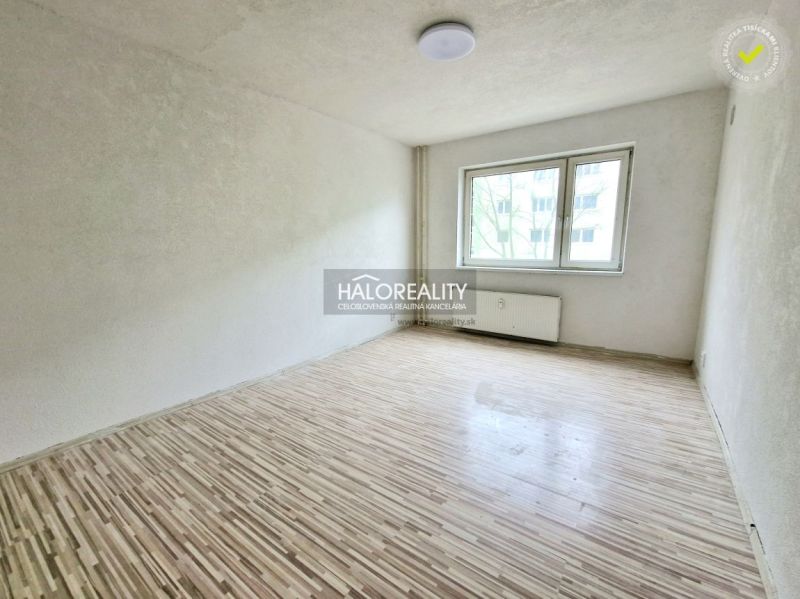 A room in a 2-room apartment with a wood-patterned floor and a white wall.