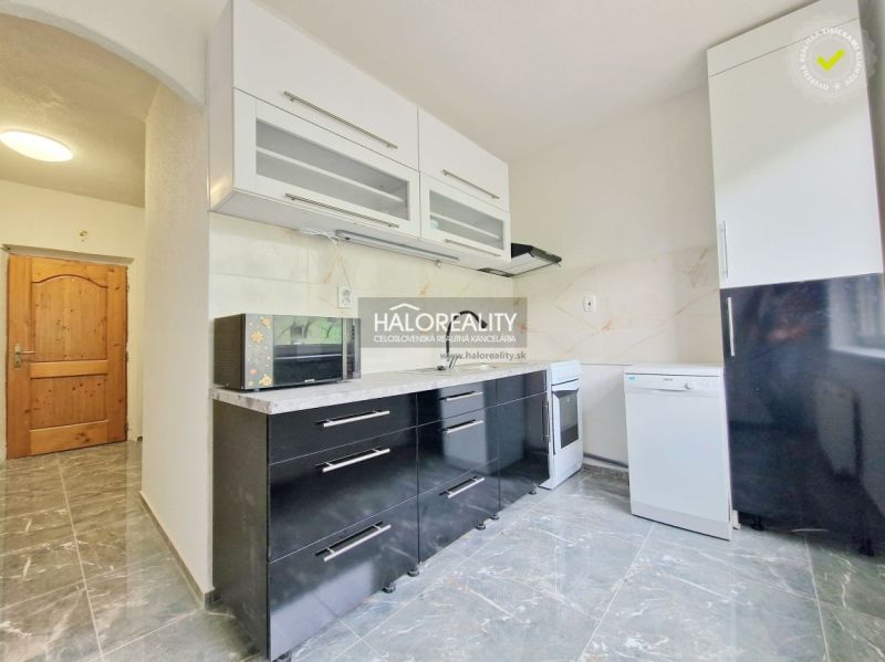 A kitchen in a 2-room apartment with black cabinets and appliances, and a floor with a wooden decor.