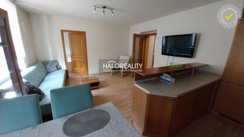 Living room in a three-room apartment with a sofa, television, and wooden decor flooring.