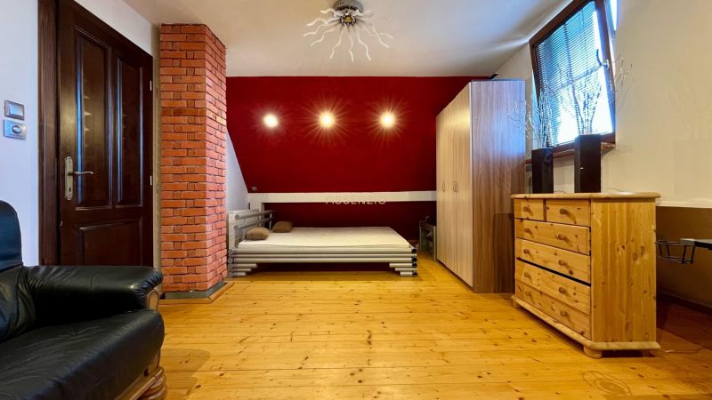 A bedroom in a family house with wooden flooring, a red wall, and furniture.