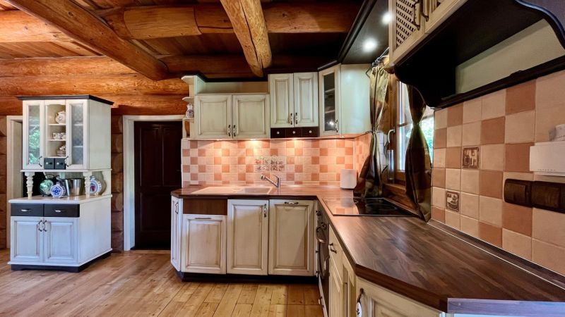 A kitchen in a family house with wooden beams, white cabinets, and tiles.
