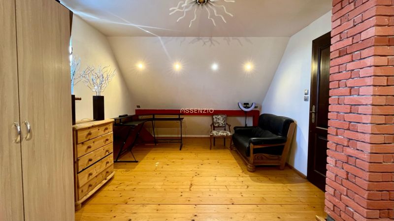 Attic room of a family house with wooden flooring, a sofa, and a brick wall.