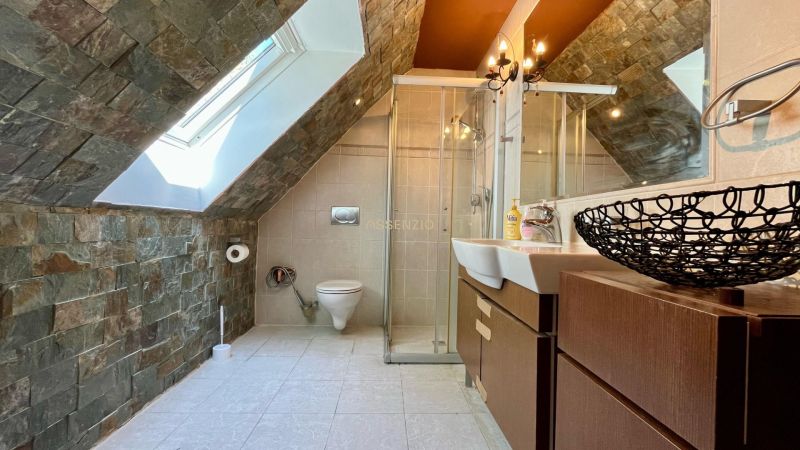 A bathroom in a family house with tiled walls, a sink, and a shower corner, attic window.