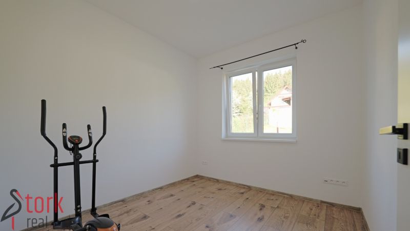 A room with a window, an exercise machine, and a wooden-decor floor in a family house.