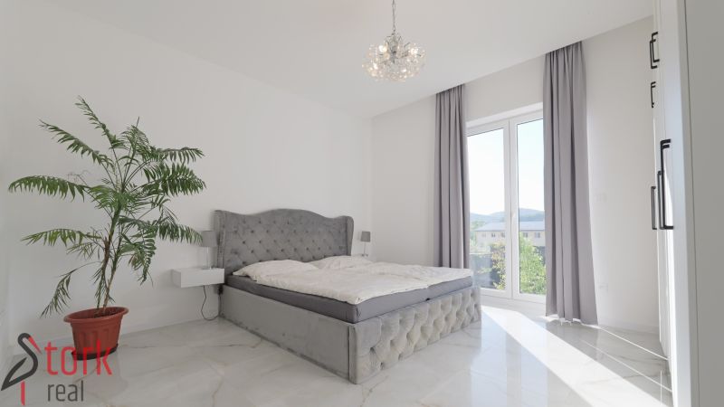 A bedroom in a family house with a gray bed, a houseplant, and ceramic flooring.