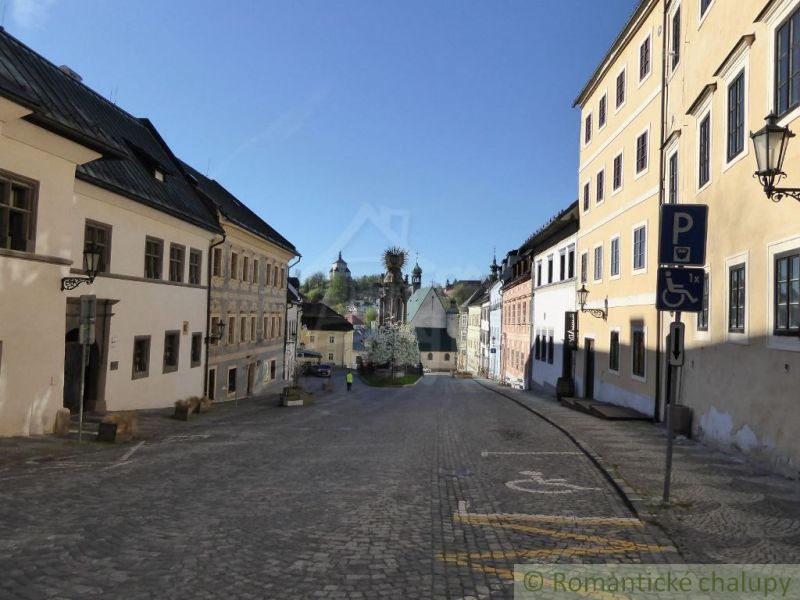 A street with historic buildings in the center of Štiavnické Bane, cobblestone pavement, and accessible parking.