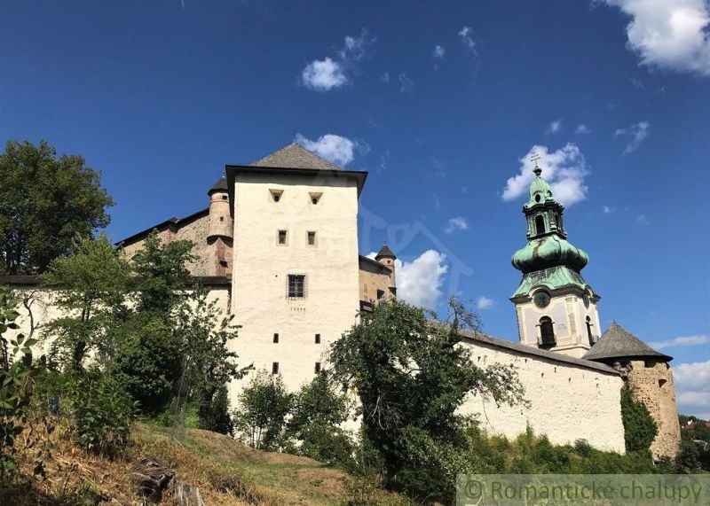 Historical architecture with a tower and a wall in Štiavnické Bane, surrounded by greenery and a blue sky.