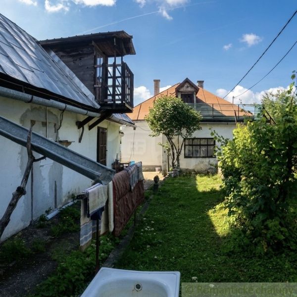 A garden with two buildings of a family house in Štiavnické Bane and a tree in the middle.