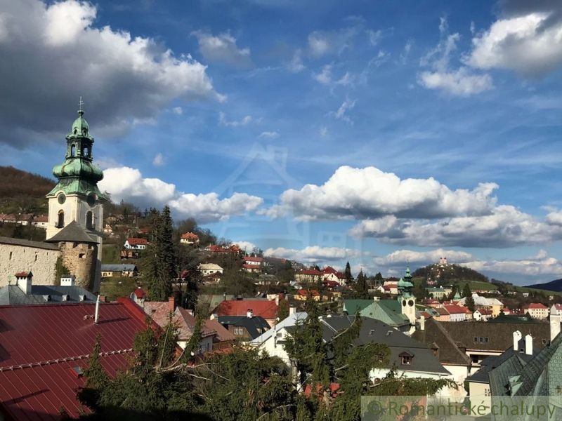 Panorama of Štiavnické Bane with the church tower, colorful roofs, and mountains in the background.