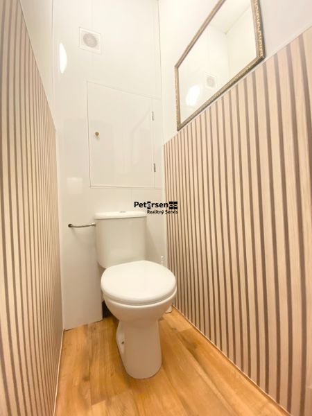 A toilet in a 3-room apartment with striped walls and a wood-patterned floor.