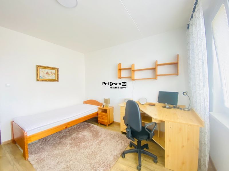 A room with a bed, carpet, table, and chair in a 3-room apartment.