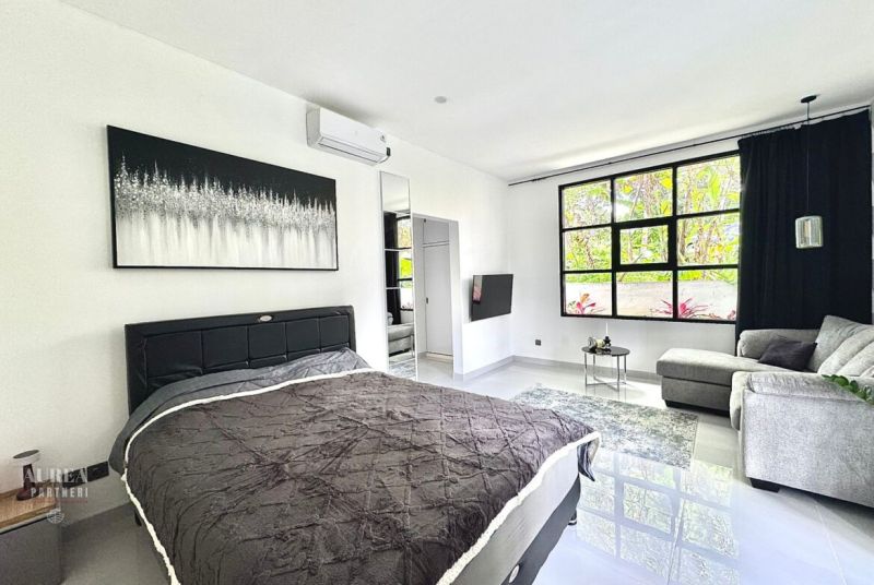 A bright bedroom with a large window, a comfortable sofa, and minimalist art on the wall.