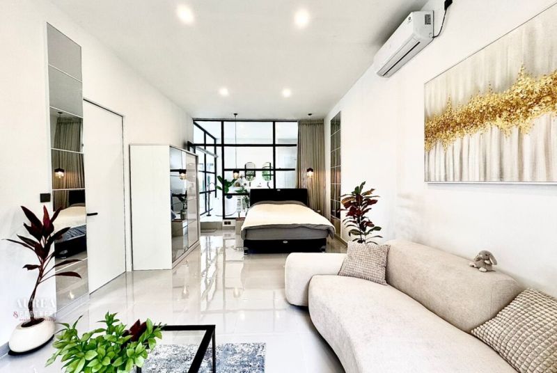 Bright living room with a bed in a villa, white walls, plants, mirror, and art.
