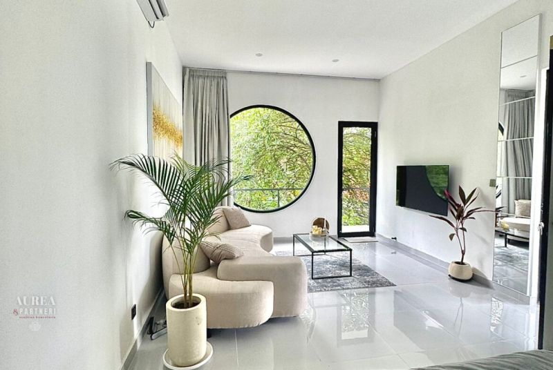 A bright living room in a villa with a large round window and plants.