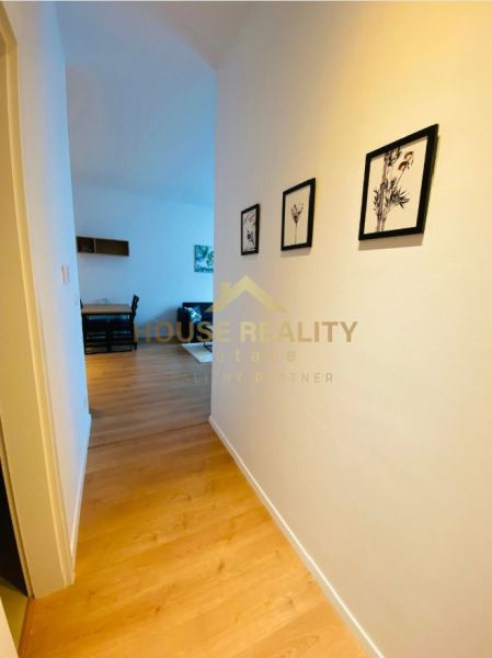 A hallway with a wooden decor floor, pictures on the wall, entrance to the living room in a two-room apartment.