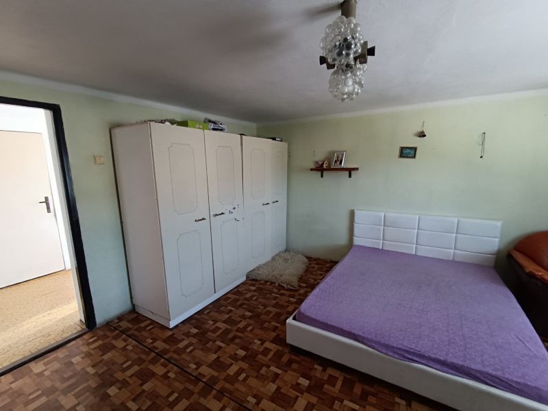 A bedroom with a white wardrobe, a bed, and a wooden decor floor in a family house.