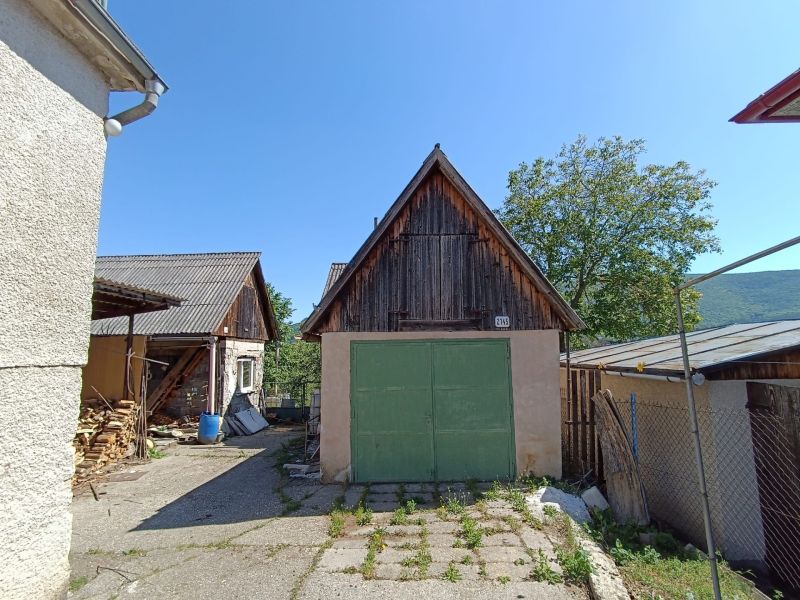 A yard by a family house in Nová Baňa with a wooden annex and trees.