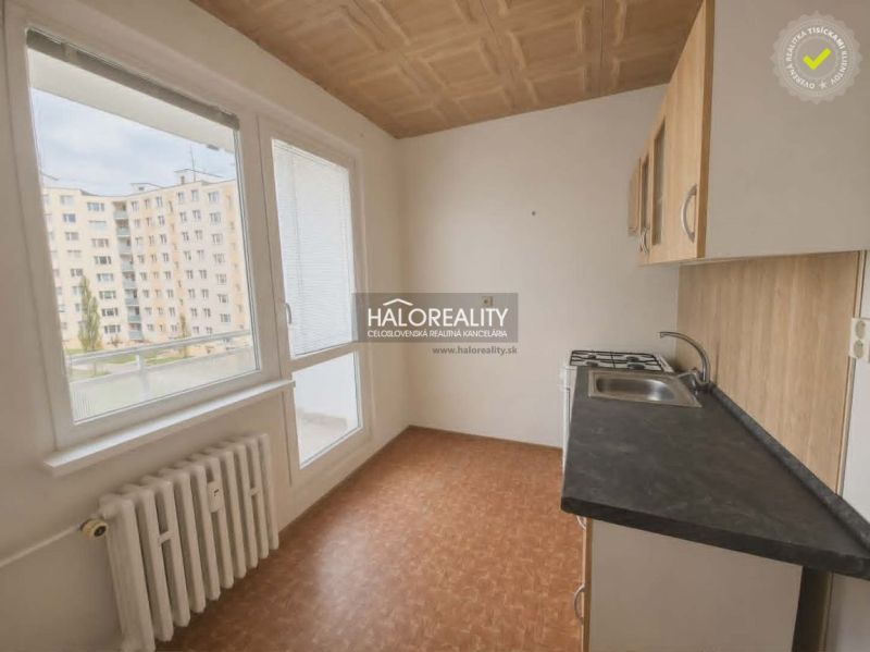 A kitchen in a studio apartment with a view of city buildings, wooden decor flooring.