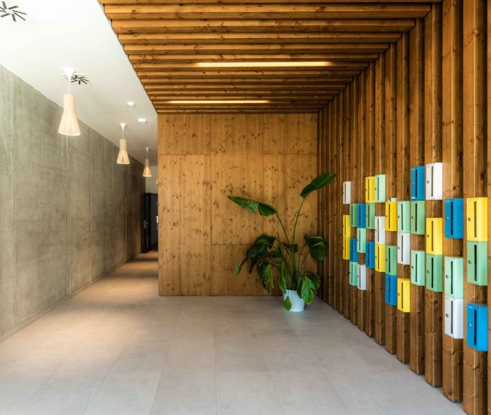 Entrance hall with wooden paneling, colorful mailboxes, and a plant.