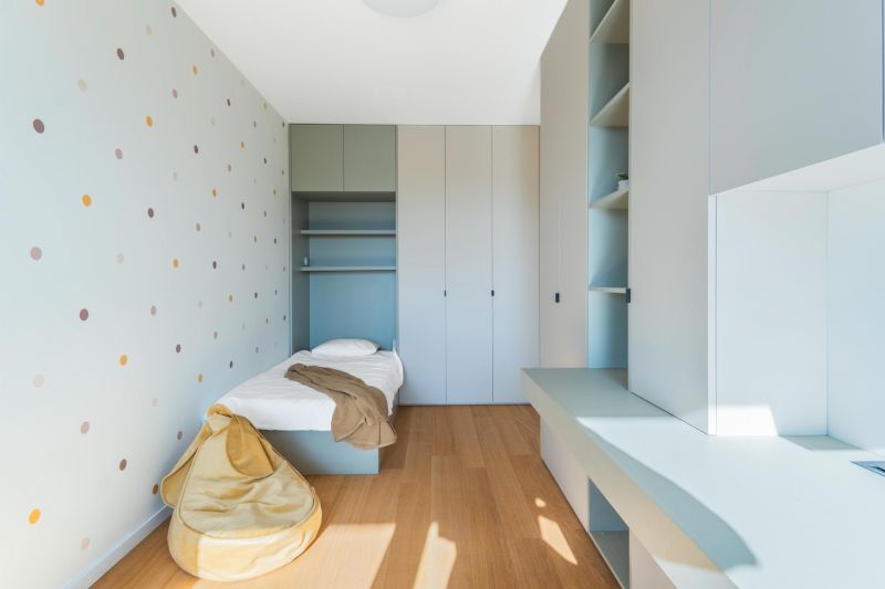 A room in a three-room apartment with a dotted wall, built-in wardrobes, and a floor with a wooden decor.