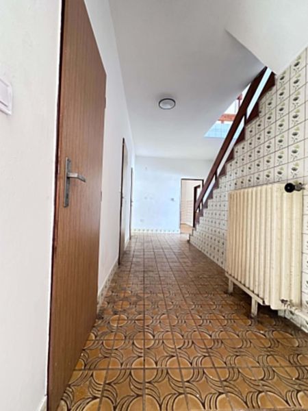 A hallway in a family house with brown tiles and a staircase.