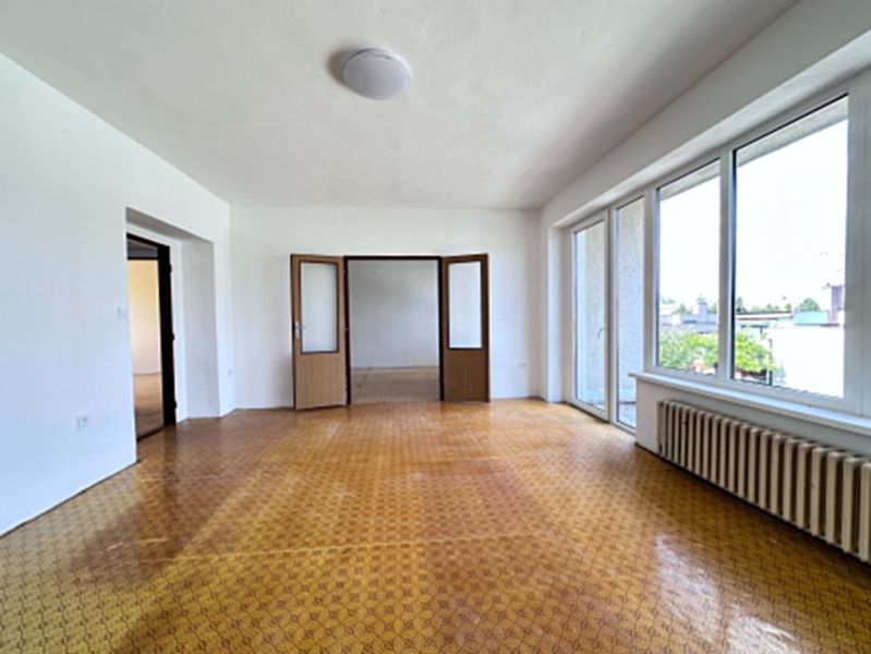 A bright room in a family house with a wood-patterned floor and large windows.