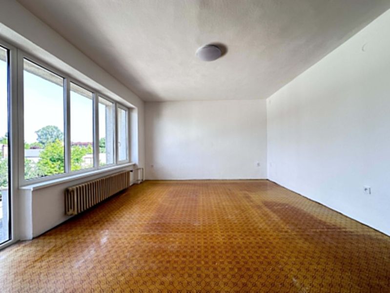A spacious room with large windows and a wooden decor floor in a family house.