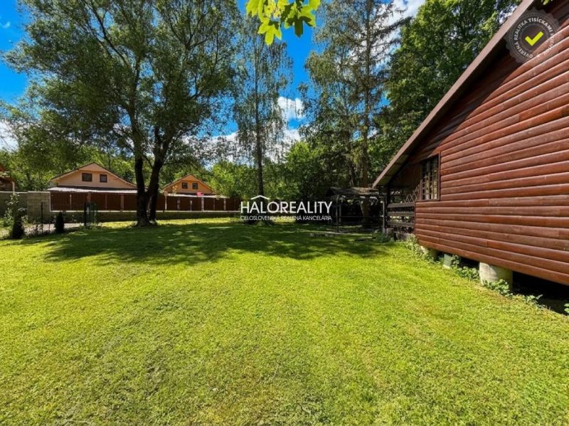 A wooden cottage in Prašice surrounded by a green lawn and trees.