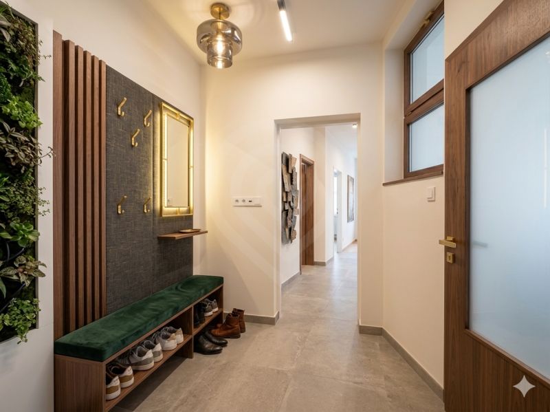 A hallway in a 3-room apartment with green plants, coat racks, and shoes on a bench.