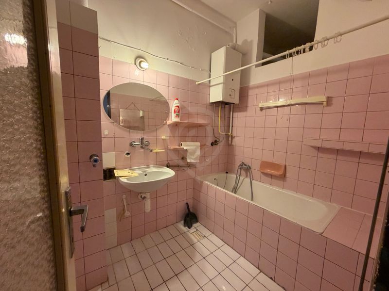 A bathroom with pink tiles, a bathtub, and a mirror in a 3-room apartment.