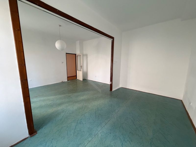 An empty room in a 3-room apartment with a floor featuring a green design and a white chandelier.