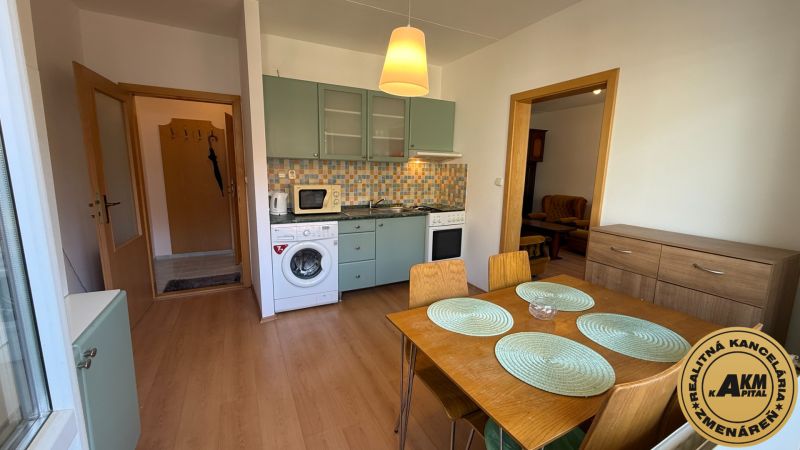 A kitchen with built-in appliances, a dining table, and a wooden decor floor in a studio apartment.