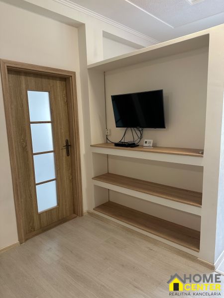 3-room apartment with a TV on the wall, shelves, and a floor with a wooden decor.