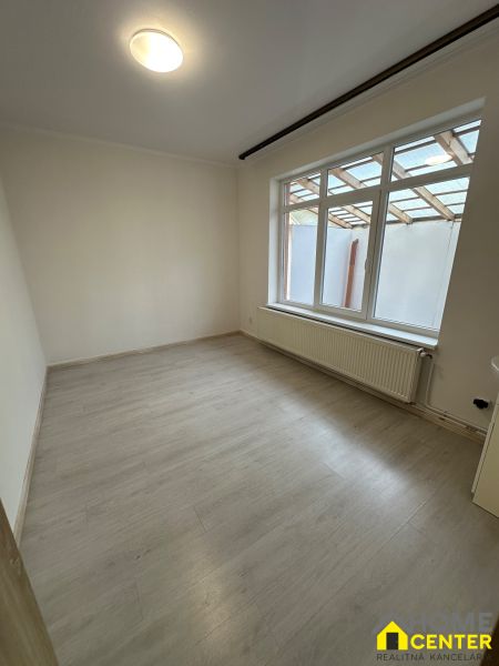 A room in a three-room apartment with a wooden decor floor, white walls, and a large window.