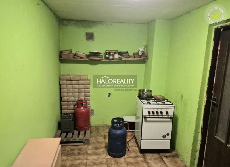 A kitchen with a stove, two propane-butane bottles, and green walls, Gardens.