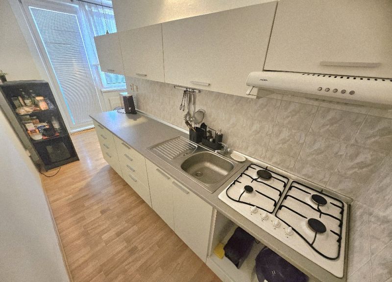 A kitchen with a gas stove and cabinets in a studio apartment, floor with wood decor.