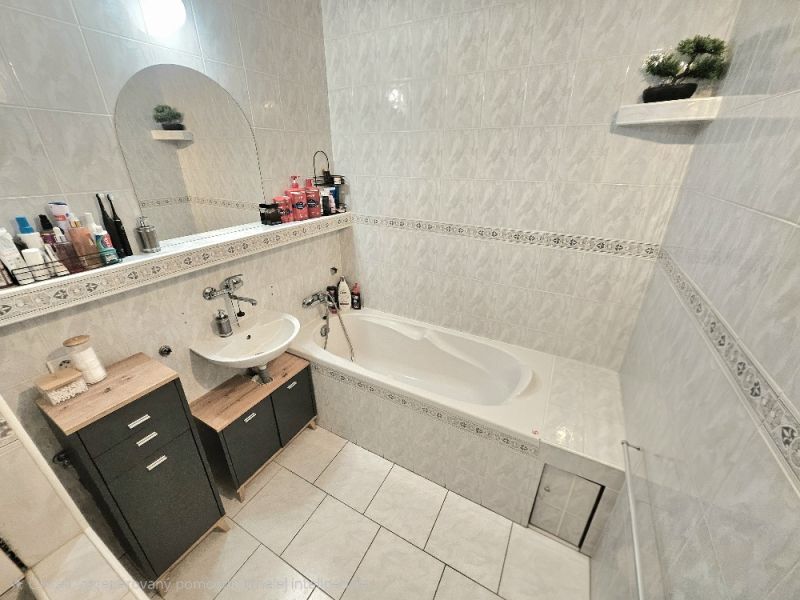 A bathroom in a studio apartment with a bathtub, sink, and storage cabinets.