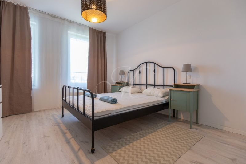 A bright bedroom with a metal bed, a lamp, and a floor with a wooden decor in a 2-room apartment.