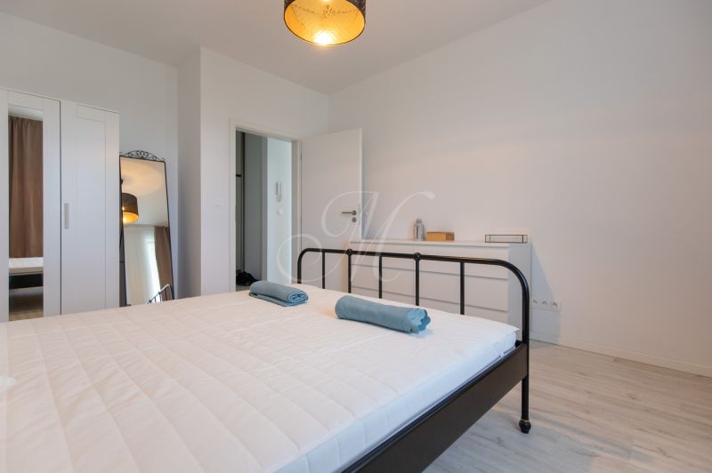 Bedroom in a 2-room apartment with a bed, mirror, and white furniture.