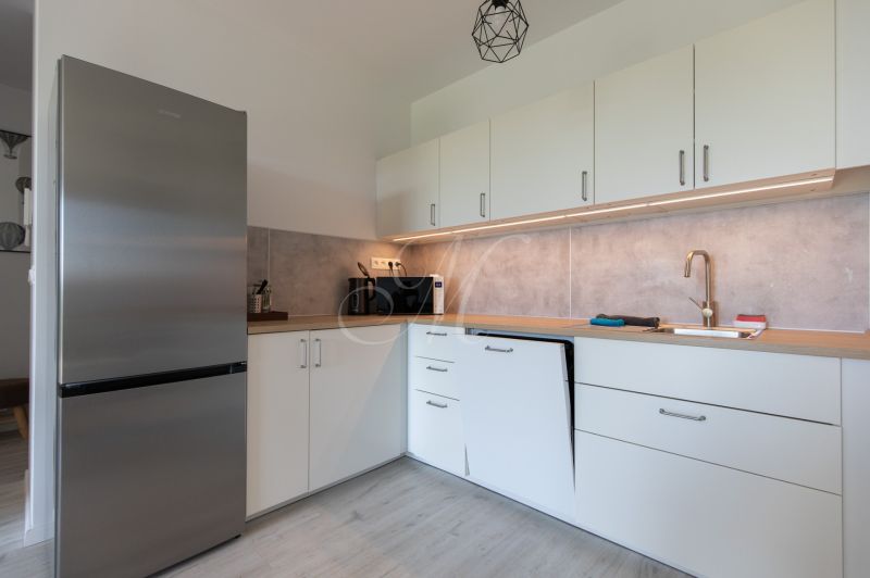A kitchen in a 2-room apartment with a stainless steel refrigerator and a wooden decor floor.