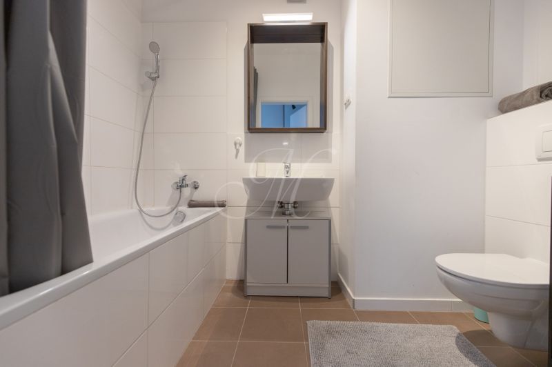 Bathroom with a bathtub, sink, mirror, and light tiles in a 2-room apartment.