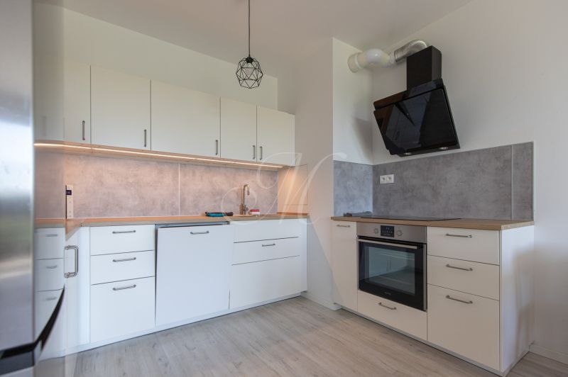 A kitchen in a 2-room apartment with a white kitchen unit and a floor with a wood decor.