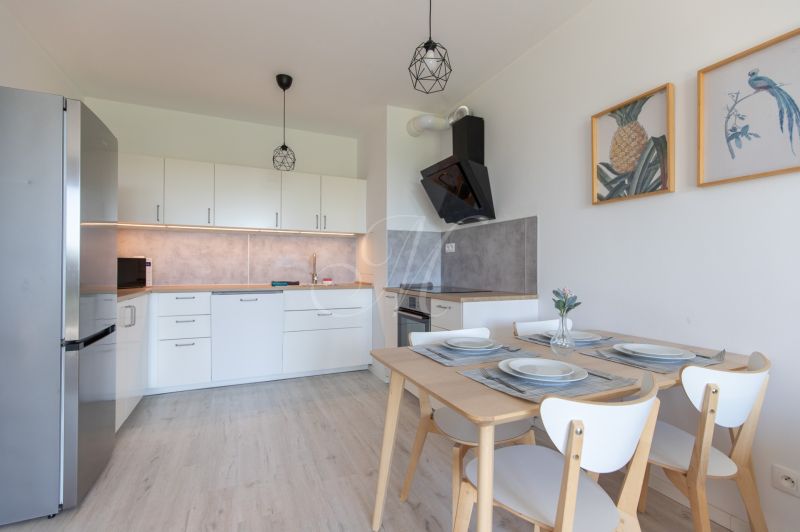 A kitchen in a 2-room apartment with a wooden decor floor, white cabinets, and a dining table.