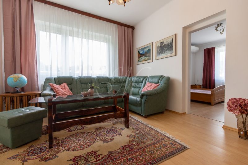 A living room with a wood-patterned floor, a green sofa, and an oriental rug in a three-room apartment.