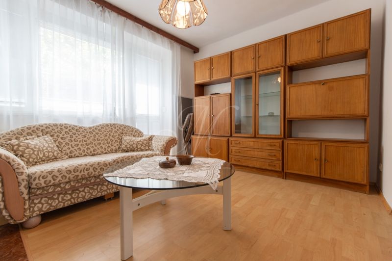 Living room in a three-room apartment with a wooden decor floor, a sofa, and a furniture set.