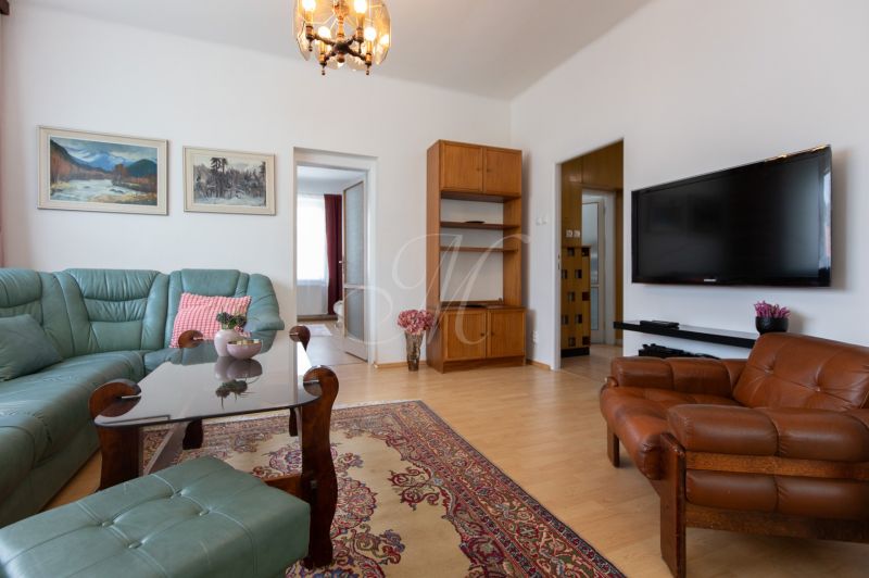 A living room of a three-room apartment with a wooden decor floor, a sofa set, and a television.